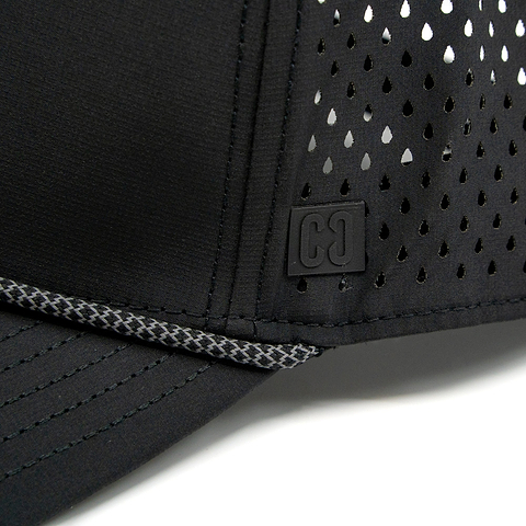 Close-up of the CORE Aero Rope Cap in black, featuring ventilated holes, prominent stitching, and a small square CORE logo patch with “C C” on the front near the brim.