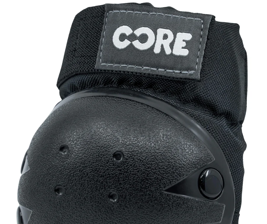 Close-up of the CORE Junior Triple Skate Protection Pad Set in black/grey, featuring a black protective knee pad with a textured hard shell, fabric strap, and a stitched rectangular "CORE" label in white at the top—ideal for skatepark safety.