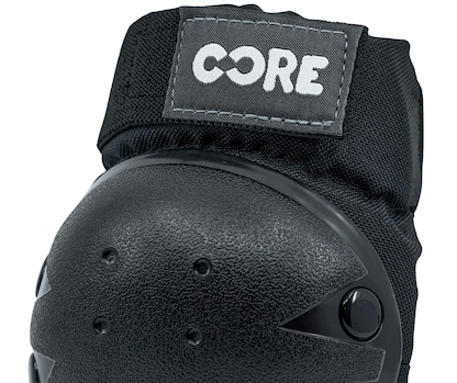 Close-up of the CORE Junior Triple Skate Protection Pad Set in black/grey, featuring a black protective knee pad with a textured hard shell, fabric strap, and a stitched rectangular "CORE" label in white at the top—ideal for skatepark safety.