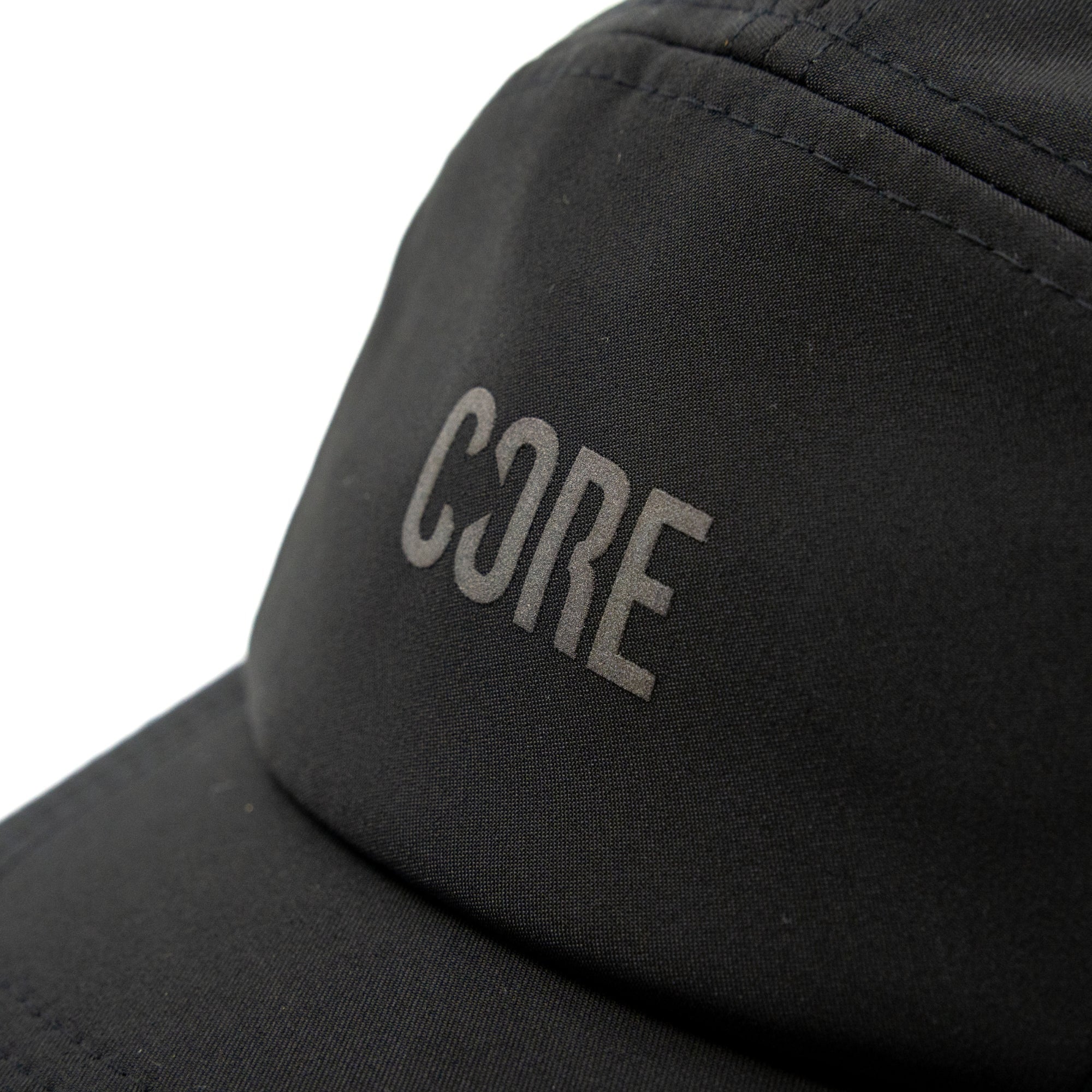 Close-up of the CORE Performance Cap in black, featuring “CORE” printed in gray with the “O” stylized as a mirrored “3.” This cap by CORE showcases subtle reflective detailing for enhanced visibility.