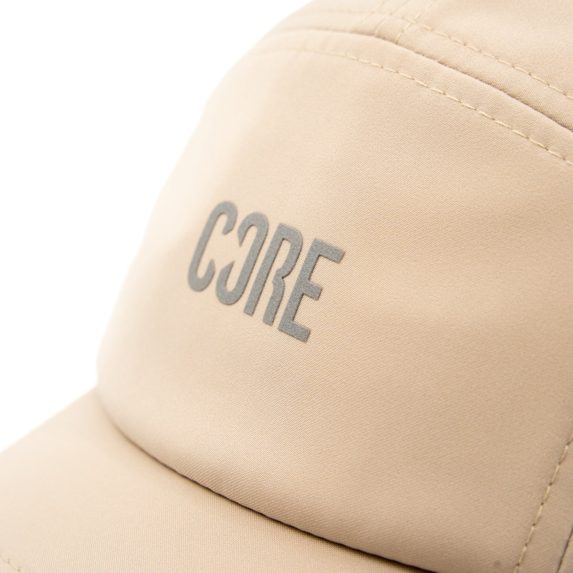 A close-up of the CORE Performance Cap in Sand / Reflective, featuring the word “CORE” in gray uppercase letters on the front panel. Crafted by CORE from breathable fabric, this cap is designed for all-day comfort.