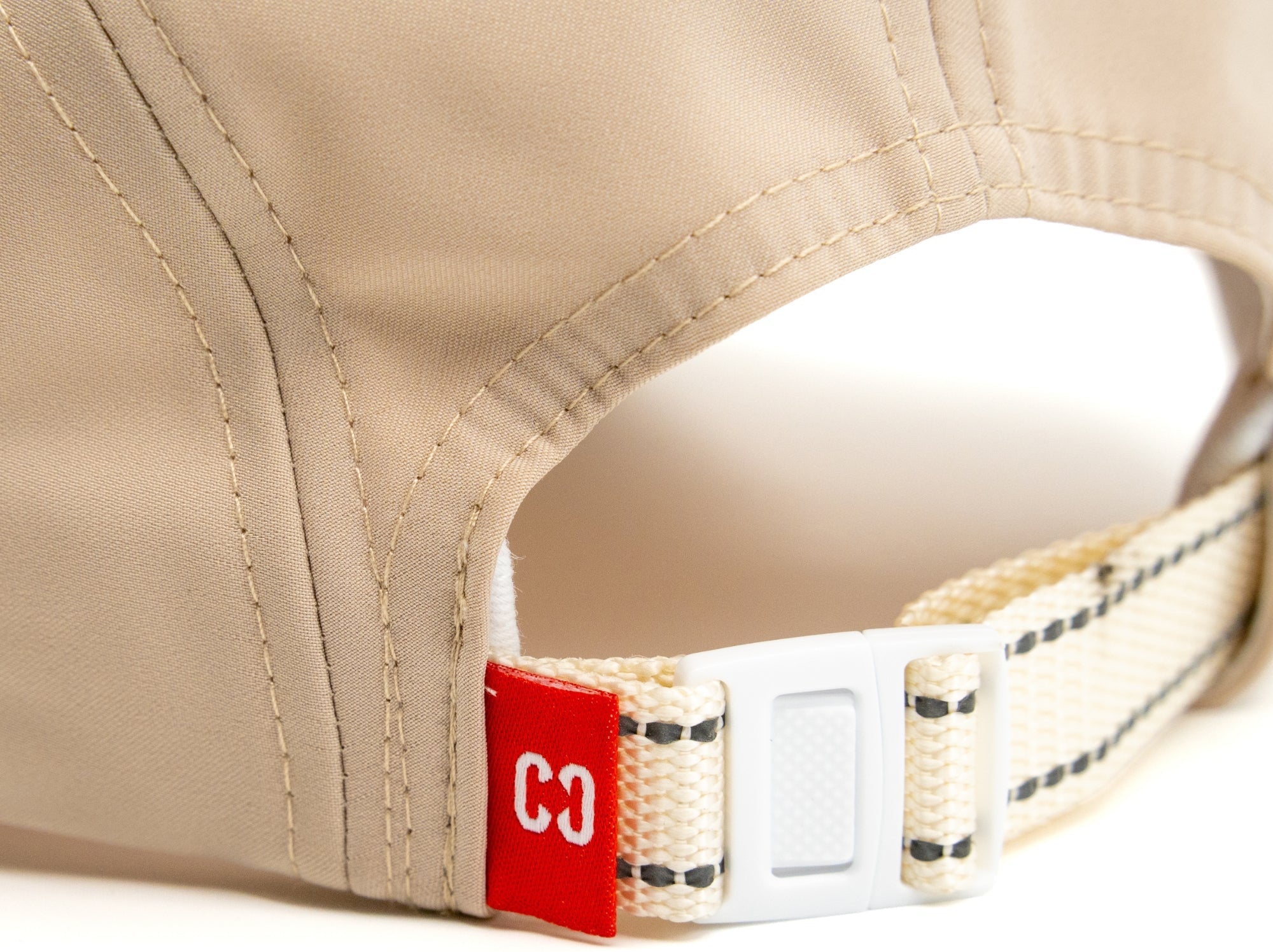 Close-up of the back of the CORE Performance Cap - Sand / Reflective, featuring a fabric strap with a plastic buckle and a small red tag displaying the number “33” in white. Crafted by CORE from breathable fabric for comfort during activity.