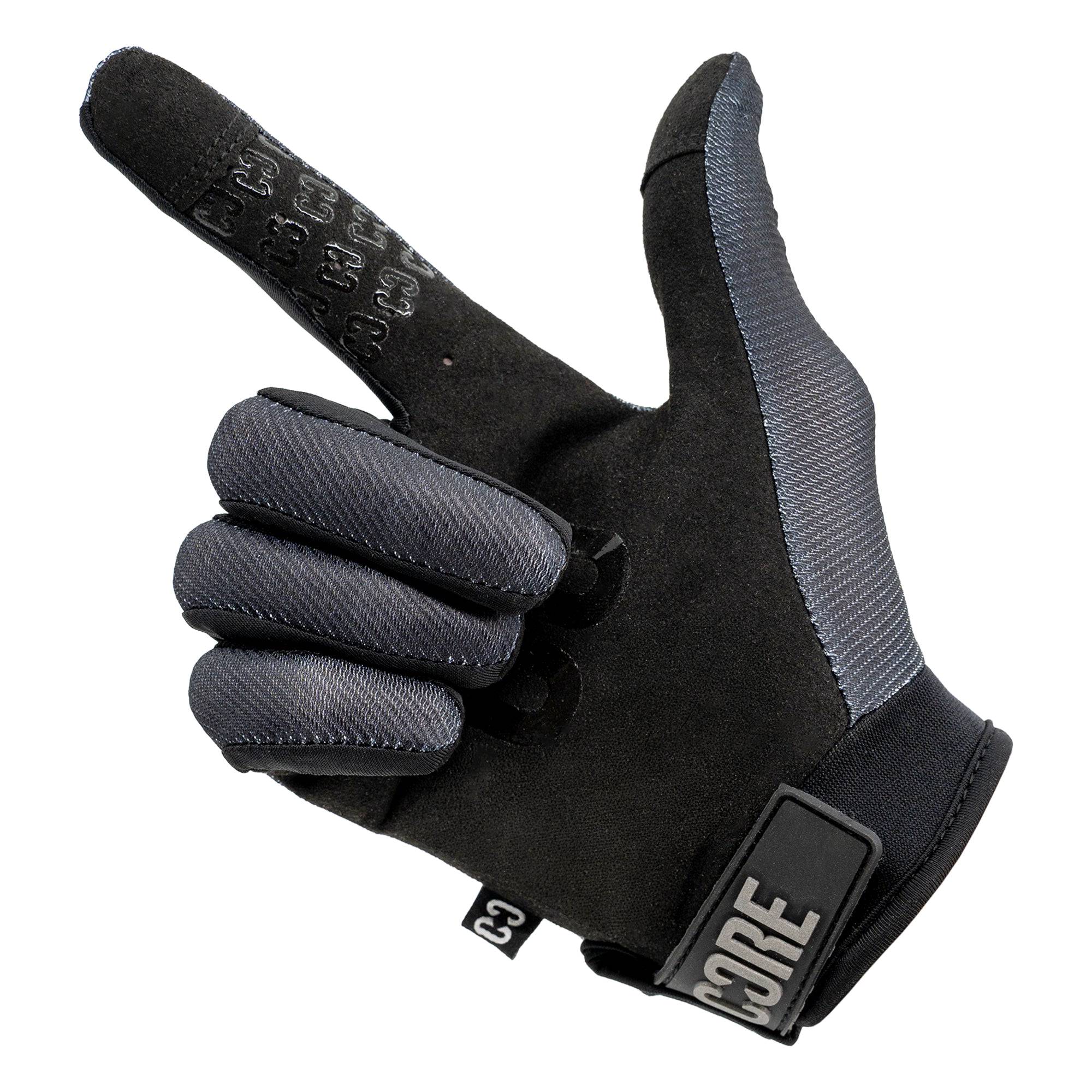 A pair of CORE Pro-Fit Velcro Skate Protection Gloves - Reflective Black by CORE is shown with the index finger pointing and the thumb extended, mimicking a hand gesture that resembles a gun or pointing. These black and gray gloves feature a reflective finish, display the CORE logo on the wrist strap, and are touch screen friendly—providing both style and functionality for riders.