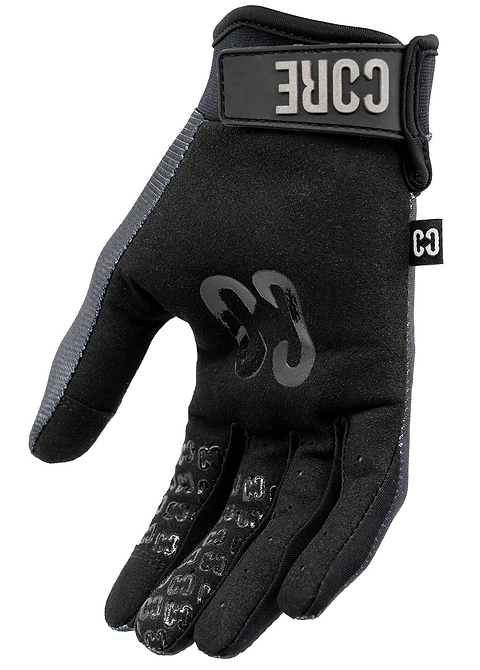 A single CORE Pro-Fit Velcro Skate Protection Glove in Reflective Black by CORE, designed for scooter riders, is shown palm up. It features a secure velcro strap, a visible CORE logo on the wrist, textured grip on the palm and fingers, and gray trim along the side.