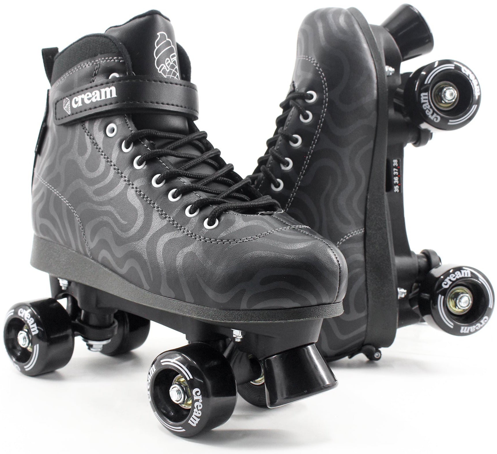 A pair of CREAM Scoop Wave Adjustable Quad Roller Skates in black, featuring vegan leather construction with a wavy gray pattern, black laces, and “CREAM” branding on the strap and wheels. Perfect for beginners, one skate is displayed upright while the other rests on its side to showcase the wheels.