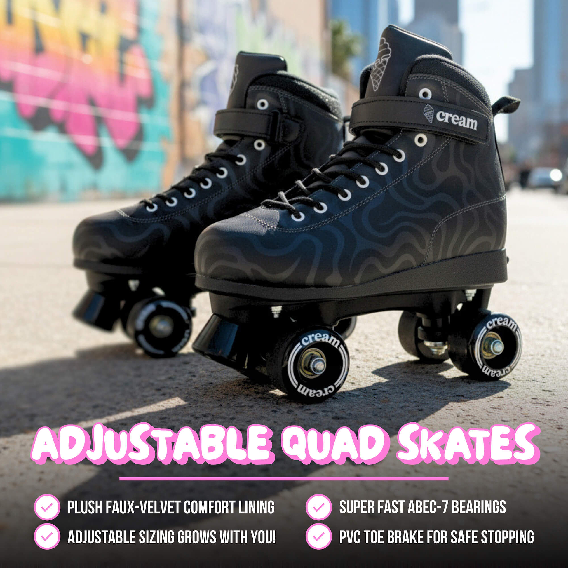 A pair of CREAM Scoop Wave Adjustable Quad Roller Skates in black on pavement, city buildings in the background. These beginner skates from CREAM feature comfort lining, adjustable sizing, ABEC-7 bearings, a PVC toe brake, and a durable vegan leather finish for stylish street skating.