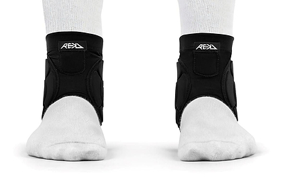 Two feet wearing white socks and black REKD Energy Covert Ankle Impact Skate Protection Guards are shown from the front on a white background. These REKD guards offer energy-absorbing protection for ankle support and stability.