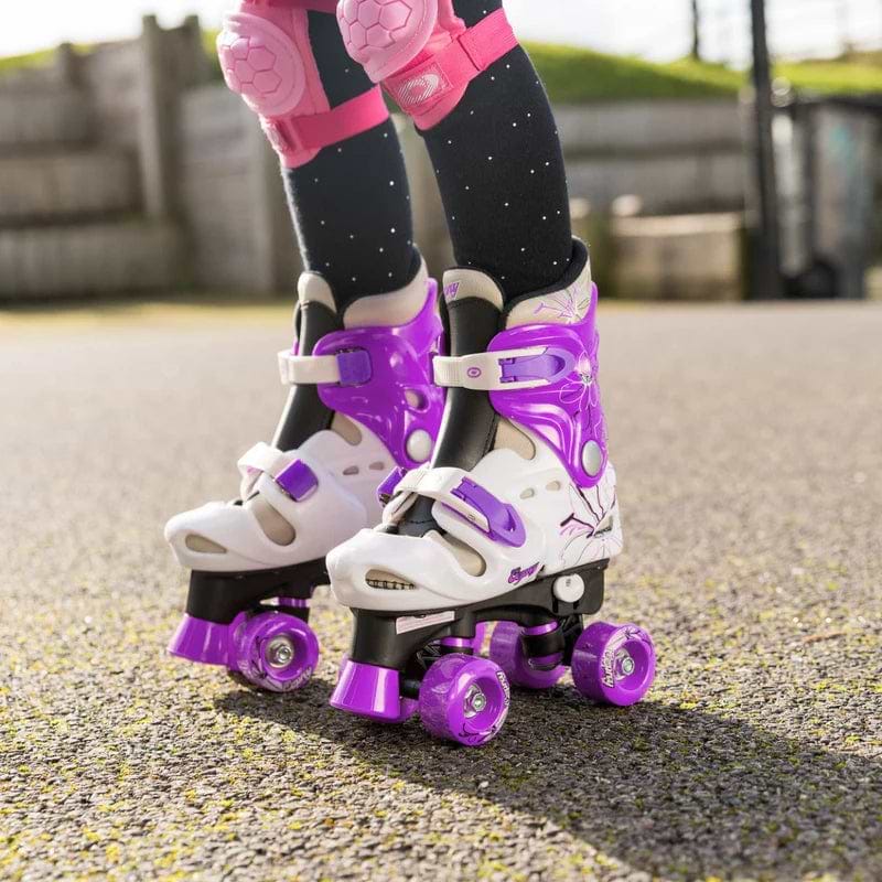 A child in black leggings with white dots and pink knee pads stands on pavement sporting the stylish Osprey Flower Adjustable Quad Roller Skates - Purple by Osprey.