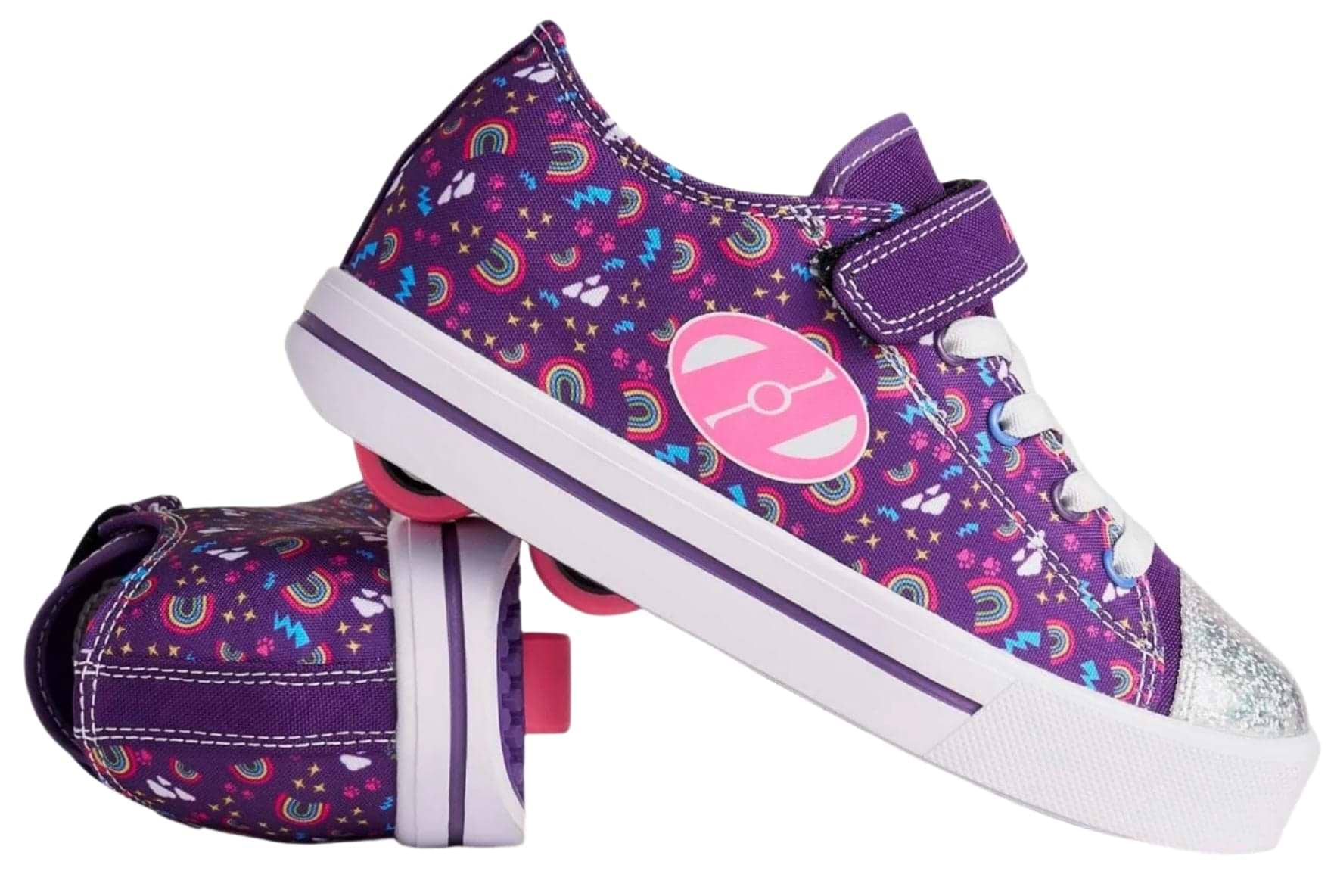 A pair of Heelys Snazzy X2 Girls Shoes in purple/multi/rainbow with star and heart patterns, white laces, purple Velcro straps, and two wheels per shoe. One shoe stands upright while the other lies on its side. Brand: Heelys.