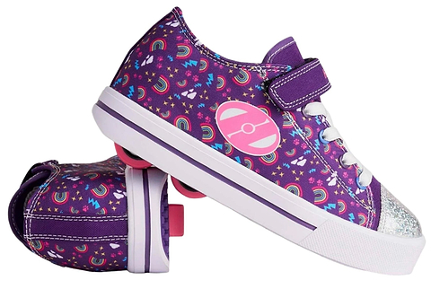 A pair of Heelys Snazzy X2 Girls Shoes in purple/multi/rainbow with star and heart patterns, white laces, purple Velcro straps, and two wheels per shoe. One shoe stands upright while the other lies on its side. Brand: Heelys.