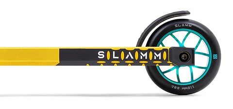 Close-up image of the rear wheel of a gold Slamm Assault Complete Stunt Scooter. The scooter features a teal and black 110mm aluminum wheel, with "SLAMM" printed on the frame and fender. The tire is marked "88A," enhancing its sleek alloy deck design.