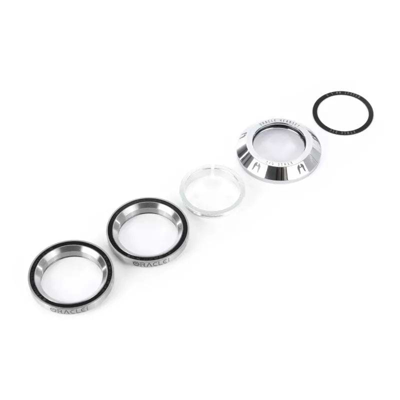 The image showcases components from the Ethic DTC Oracle Integrated Stunt Scooter Headset - Chrome, featuring a combination of metal and glass rings along with black rubber ones, all arranged in a line on a white background. These parts are specifically designed by Ethic to minimize friction in stunt scooters.