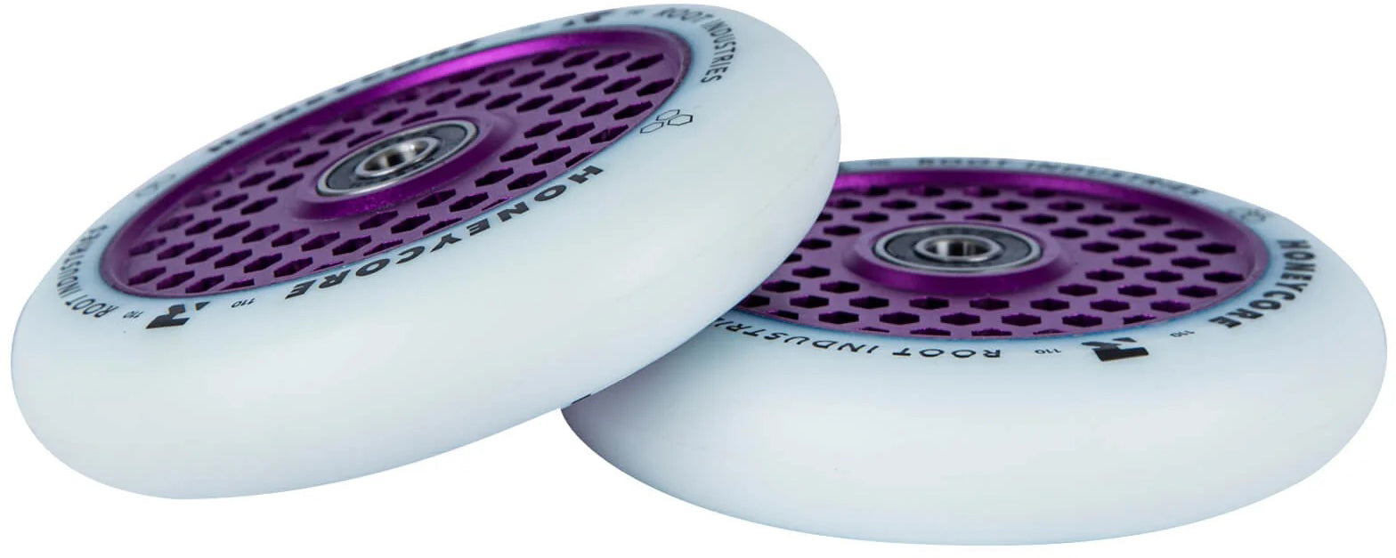 A pair of Root Industries Honeycore 110mm Stunt Scooter Wheels in white with purple honeycomb-patterned metal cores are stacked at an angle on a white background. The wheels feature black text around the outer rim and ball bearings in the center, highlighting the iconic Root Industries design.