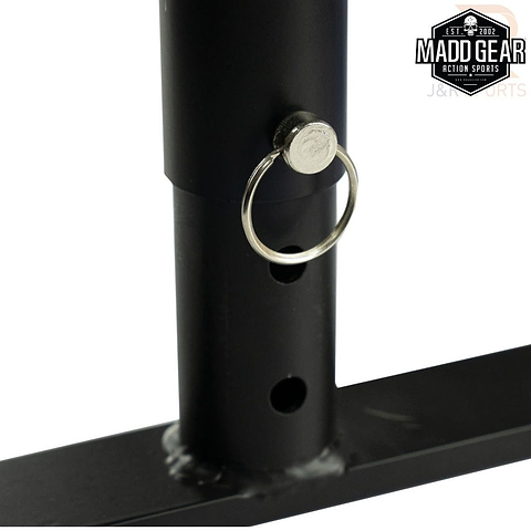 Close-up of the Madd Gear MGP Fifty5 Grind Rail - 140cm shows a locking pin inserted into one of its holes on the black metal rod, essential for perfecting grind tricks. This rail is part of a larger metal structure set against a white background, with the "Madd Gear" logo in the top right corner hinting at the adrenaline rush from skateboarding and more.