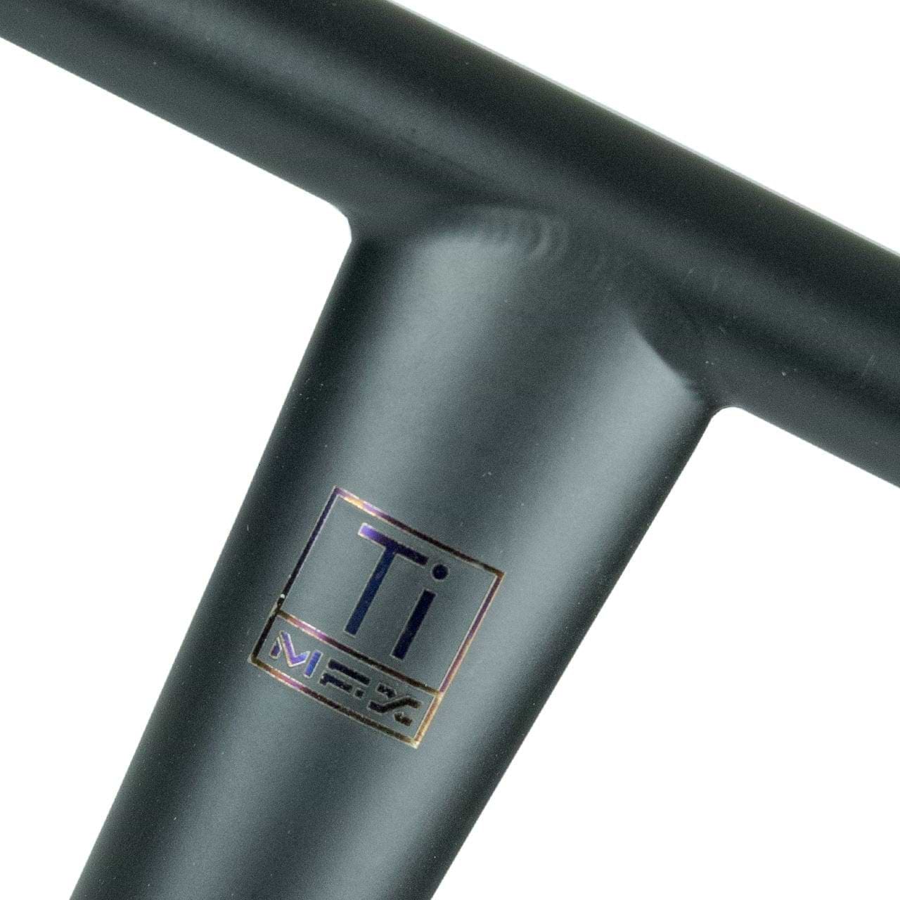Close-up of a metallic structure with a weld and a small label. The label features the letters “Ti” and the Madd Gear (MGP) logo beneath it, indicating it's the MGP MFX BAMF Titanium Oversized HIC Stunt Scooter Bar. The metal has a matte black finish with an iridescent sheen at the joint, reminiscent of oversized compression systems.