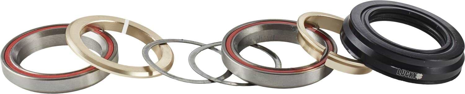 A row of various metal and plastic rings, featuring durable thrust bearings and seals for an integrated scooter headset, are aligned horizontally. Some rings have red inner linings, and one black seal prominently bears the "Lucky" branding from the Lucky Revo Integrated Stunt Scooter Headset - Black.