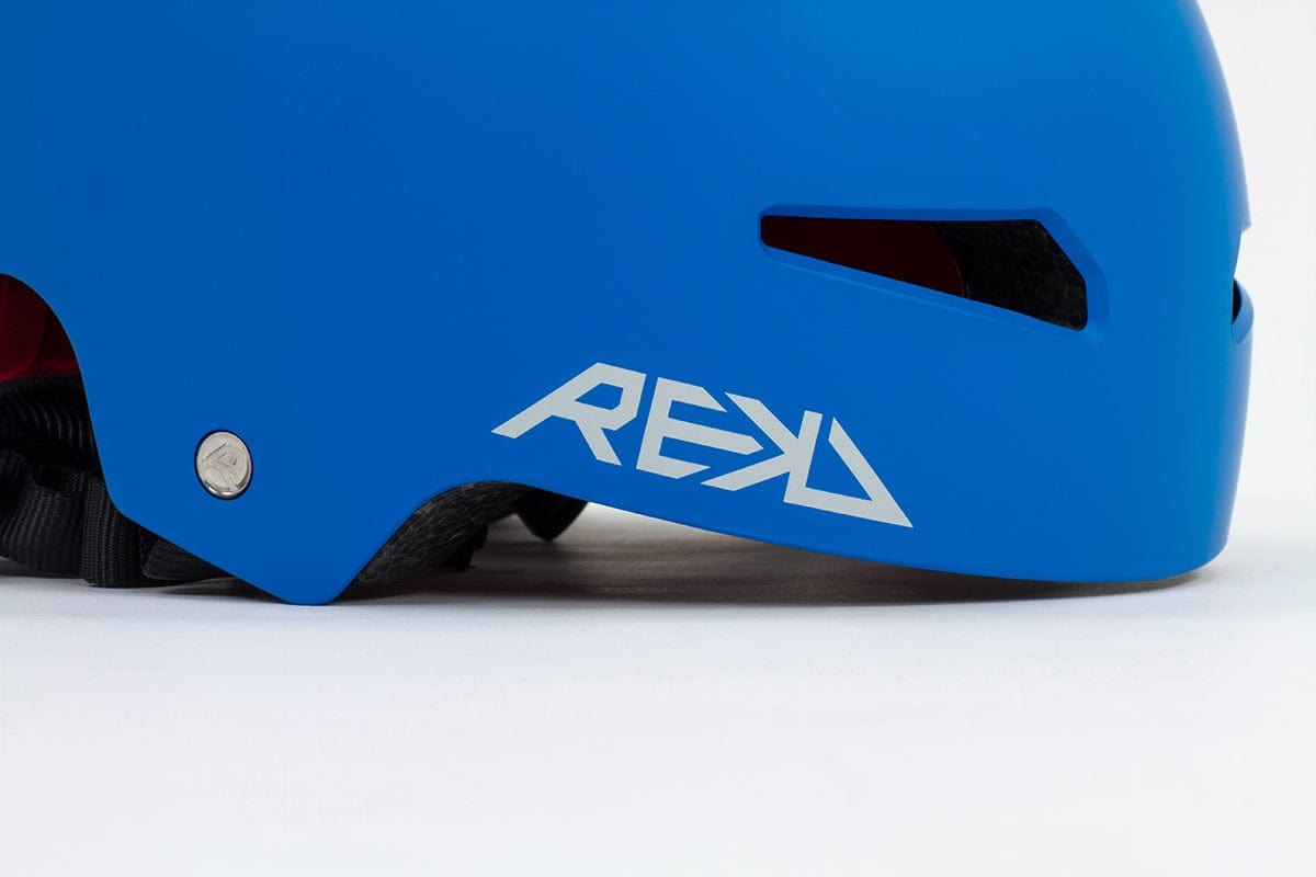 The REKD Elite 2.0 Skate / Scooter Helmet in blue features a sleek design with ventilation slots, perfect for action sports enthusiasts. The side of the helmet prominently displays the white "REKD" logo, while a black adjustable strap underneath guarantees a secure fit.