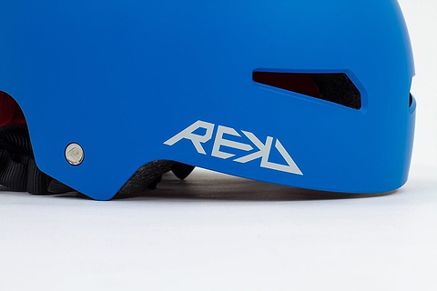 The REKD Elite 2.0 Skate / Scooter Helmet in blue features a sleek design with ventilation slots, perfect for action sports enthusiasts. The side of the helmet prominently displays the white "REKD" logo, while a black adjustable strap underneath guarantees a secure fit.
