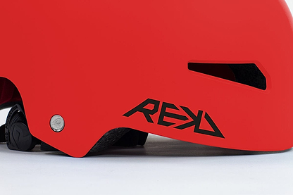 Close-up of a vibrant red REKD Elite 2.0 Skate/Scooter Helmet featuring a sleek black ventilation slot. The side prominently displays the "REKD" logo in bold black letters. Positioned on a light surface, this cutting-edge action sports helmet combines modern design with maximum safety and style.