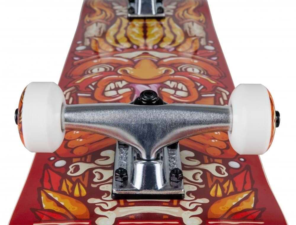 Close-up of the Rocket Chief Pile-Up Red Complete Skateboard (7.75" x 31") for beginners, featuring white wheels, aluminum trucks, a 7-ply hardrock maple deck, and an intricate orange and yellow face graphic.
