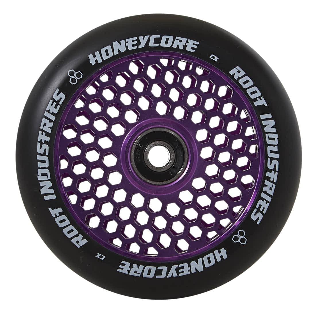 The Root Industries Honeycore 120mm Stunt Scooter Wheel in black and purple is displayed, showcasing an eye-catching honeycomb design. The inner core highlights the distinctive pattern, with "Honeycore Wheels" and "Root Industries" tastefully printed in white around the outer edge.