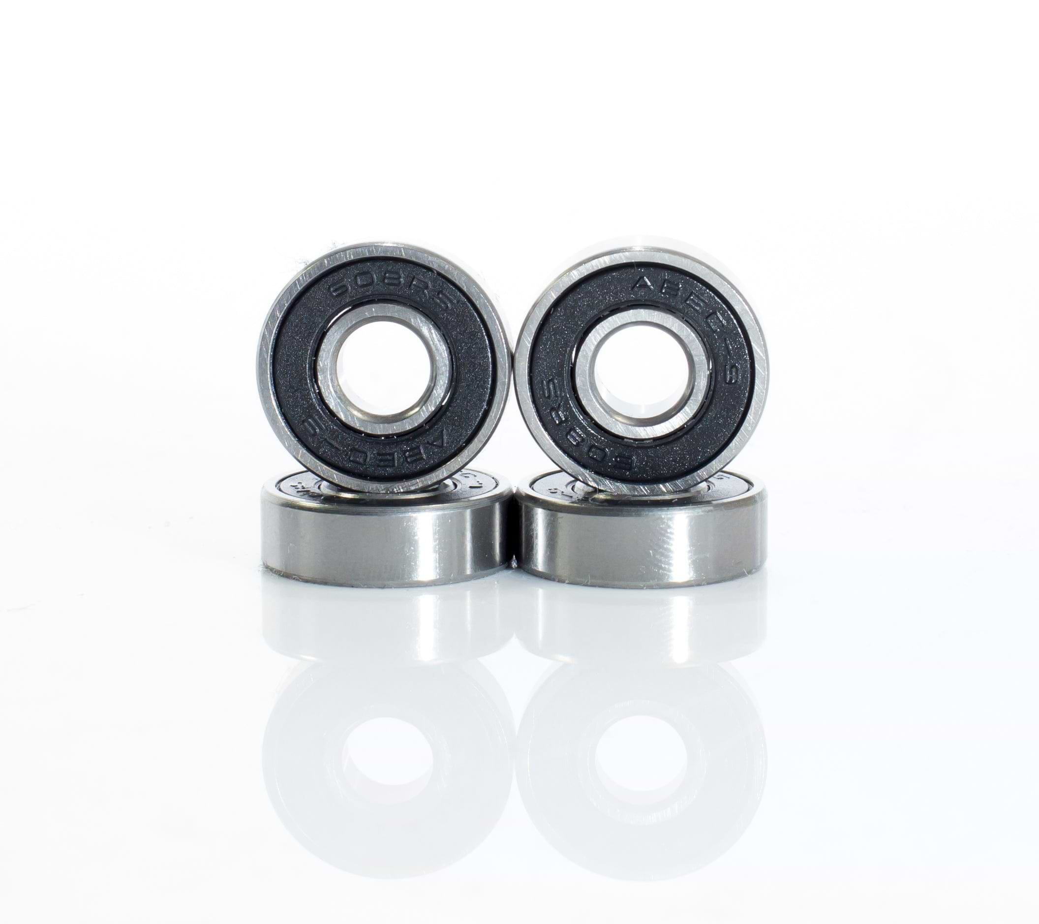 Four Skates.co.uk ABEC 9 Black Scooter Bearings, similar to those in a stunt scooter, are displayed in a staggered line with two standing and two lying flat. The metallic bearings showcase black inner rings against a simple white background, suggesting precision akin to their ABEC 9 ratings.