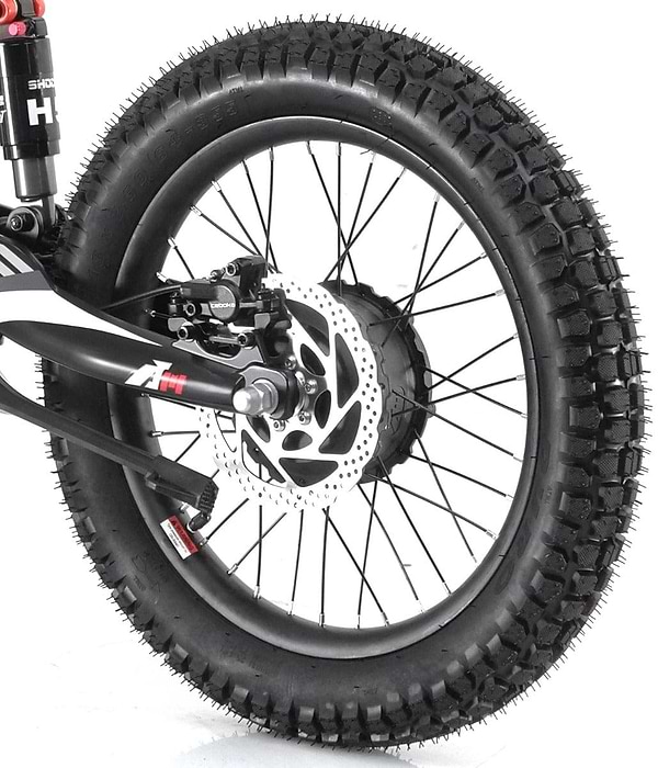 Close-up of a black bicycle wheel featuring thick, knobby tires and hydraulic disc brakes. The spokes are black, and the bike's frame is partially visible with a suspension fork, closely resembling the robust design found in the Revvi 18" Kids Electric Balance Bike - Green.