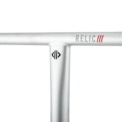 Close-up of the Drone Relic 3 Steel Oversized SCS Stunt Scooter Bars in a raw finish, featuring a silver T Bar handlebar crafted from durable Chromoly 4130 steel. The brand name "RELIC" is prominently displayed in red and gray letters, while a small Drone logo sits below the joint on the metallic surface, accented by visible weld marks.