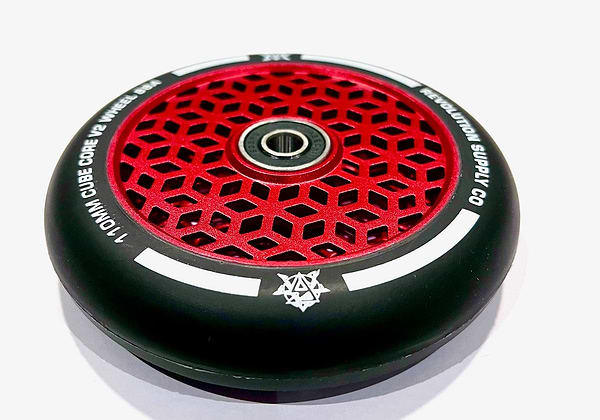 Introducing the Revolution Cubed Core Ultralite 110mm Stunt Scooter Wheel in Red, featuring a striking red and black geometric pattern. This wheel boasts the Cubed Core Ultralite design from Revolution Supply and includes a central bearing. White text encircles the mostly black outer rim, highlighting additional design elements.