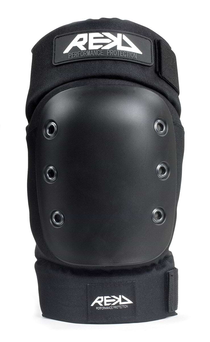 Close-up of the REKD Pro Ramp Skate Protection Knee Pads in black, showcasing a durable hard shell and metal rivet details. These knee pads feature the "REKD" logo and "Performance Protection" text on a fabric strap near the top. The ergonomic design includes knee recesses and adjustable Velcro straps to ensure a secure fit.