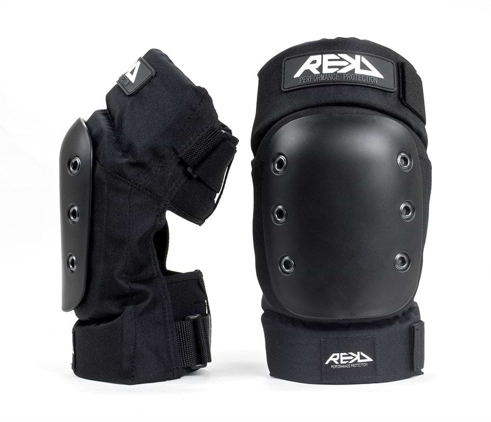 The REKD Pro Ramp Skate Protection Knee Pads in black include two knee pads, each designed with a hard outer shell and impact pro caps. The adjustable straps provide a secure fit, while the branding "REKD Performance Protection" is prominently displayed on each pad. One knee pad is positioned upright, and the other leans to the side, showcasing its ergonomic knee recesses from various angles.