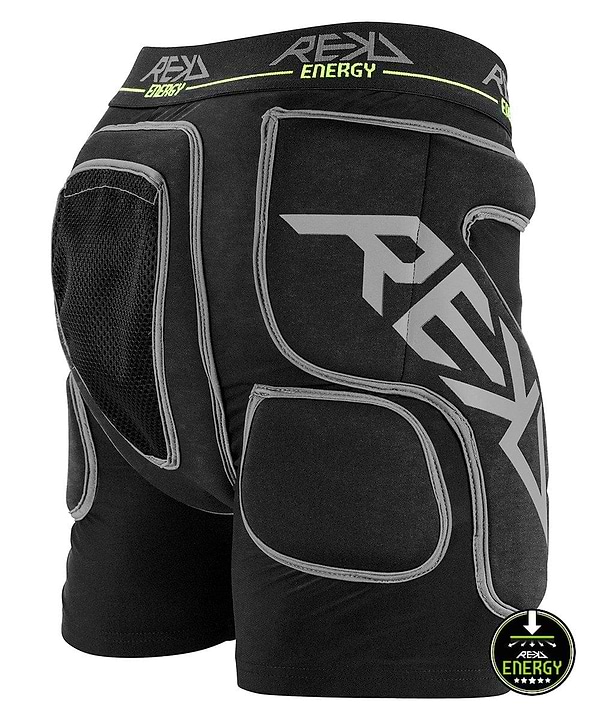 Introducing the REKD Energy Impact Skate Protection Shorts - Black: These padded protective shorts are designed with gray details and feature prominent "REKD" branding. They include mesh fabric on the hip area and a coccyx bone protector to ensure maximum impact protection. The waistband is adorned with a green "Energy" logo, and the lower right side showcases a distinctive downward arrow rating emblem.