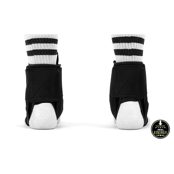 Rear view of two feet wearing REKD Energy Covert Ankle Skate Protection Braces in black over white socks with black stripes. A circular badge on the bottom right corner showcases the words "REKD Energy," highlighting enhanced ankle protection along with a stylized mountain graphic.