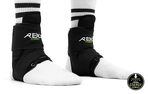 A person is wearing REKD Energy Covert Ankle Skate Protection Braces in black over white socks with black stripes. These supports, branded under "REKD," ensure maximum ankle protection. The logo in the bottom right corner proudly displays the bold REKD branding, reaffirming their commitment to quality and support.