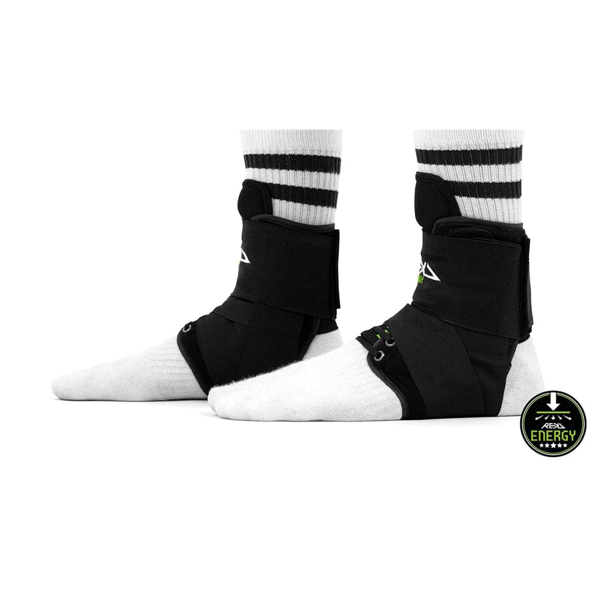 Two feet in white socks are equipped with REKD Energy Covert Ankle Skate Protection Braces in black, providing robust ankle support with laces and straps. These braces showcase the REKD logo featuring a mountain design, and a small circular "Energy" logo with the same motif is elegantly placed in the corner for a finishing touch.
