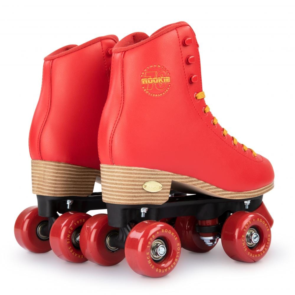 A pair of Rookie Classic 78 Quad Roller Skates in bright red, featuring wooden heels, vegan-friendly materials, red wheels, and yellow laces. The Rookie brand logo is visible on the side of the ankles. The skates are set against a white background.