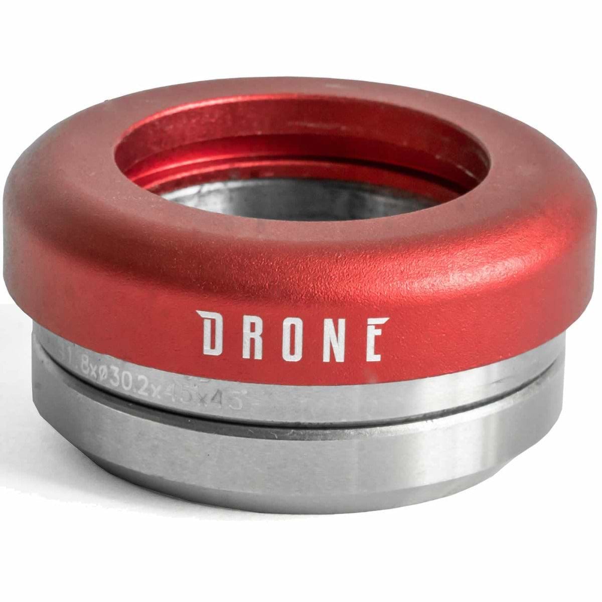 A red and silver metal component from the Drone brand, specifically the Drone Synergy 2 Integrated Stunt Scooter Headset, is crafted from 6061 aluminum. The word "DRONE" is printed on it, and it showcases cylindrical shapes with inner grooves similar to those of a stunt scooter headset. It includes smooth bearings and is displayed against a white background.