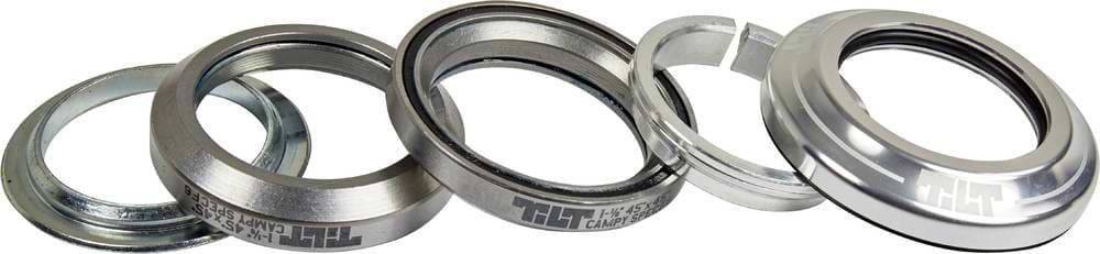 Five Tilt Integrated Stunt Scooter Headset bearings and spacers by Tilt are arranged at an angle, showing engraved text; these silver campy spec components with anodized dust covers are essential for scooter headsets, pictured on a white background.