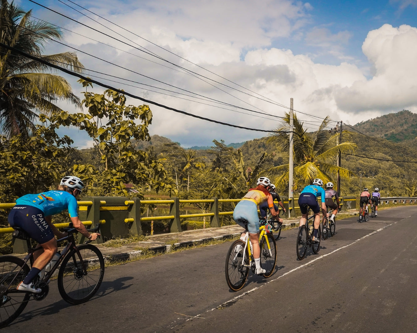 Cyclists ride away from the camera on a country road in Indonesia