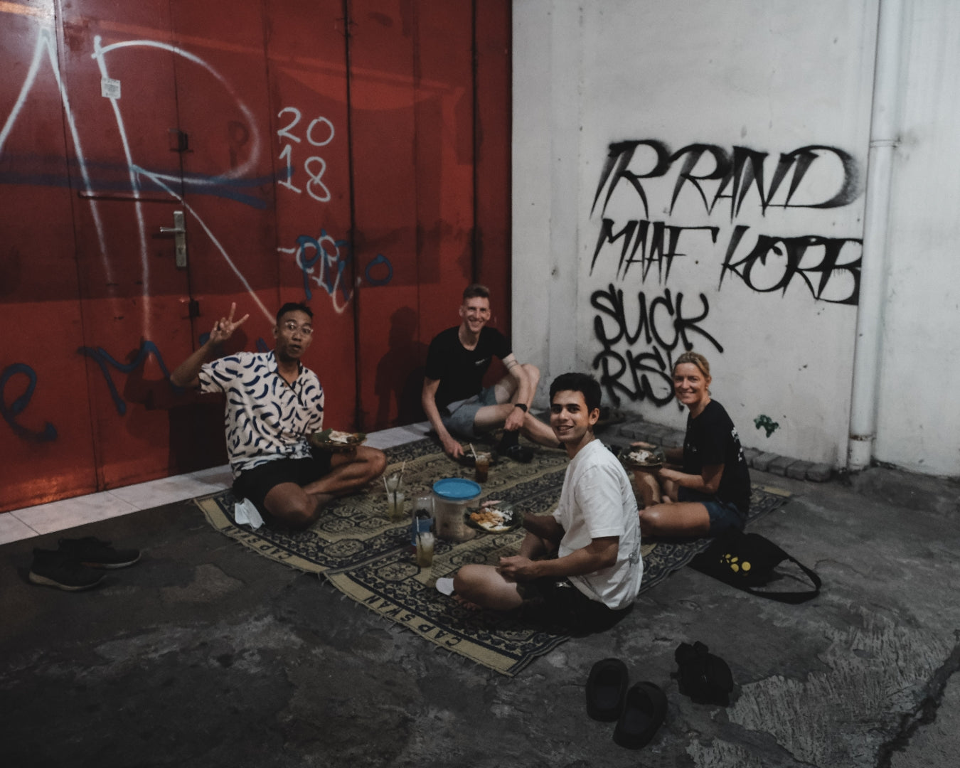 A group of people all sitting on the ground at night, eating a shared meal