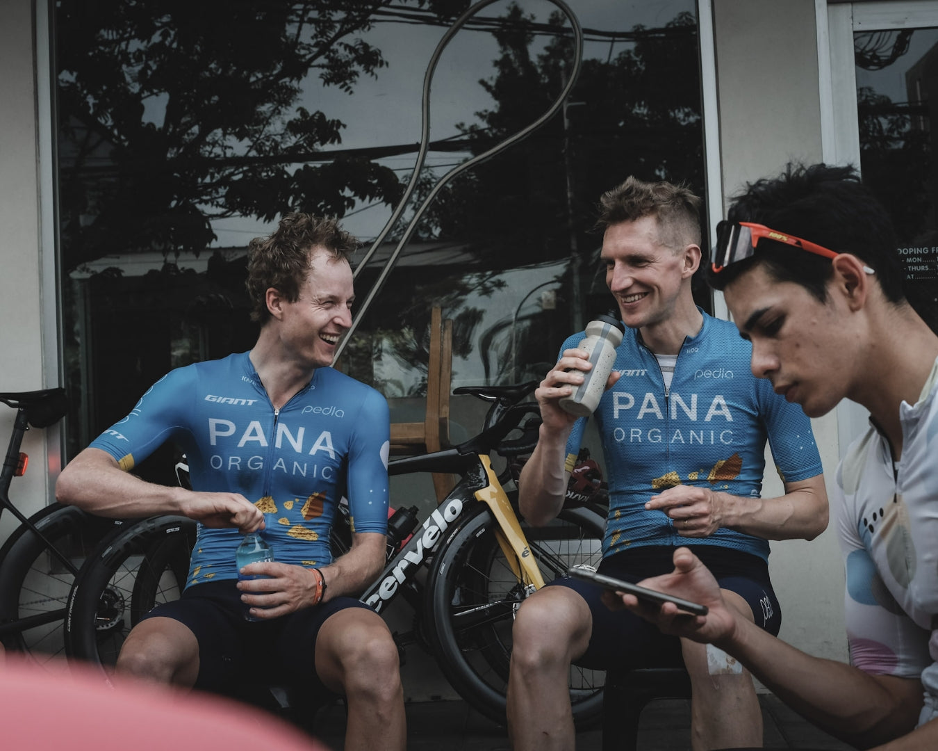 Two Pana Organic riders laugh while taking a break from the bike, sitting down and drinking