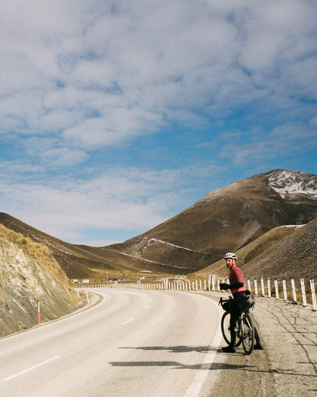 A rider looks back at the camera, stopped on the side of the road in a mountain pass.