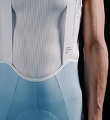 Close-up of men's Pedla SuperFIT 2.0 powder blue full-length cycling bib tights with white breathable mesh bib, Elastic Interface chamois, reflective logos, ergonomic seams and premium Italian fabric for aerodynamic support