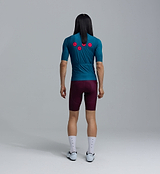 Men's classic teal cycling jersey back view on rider, LunaLUXE performance jersey, SPF50 breathable, moisture-wicking, four-way stretch, extended sleeves, low-cut collar, silicone hem gripper; paired with burgundy cycling shorts