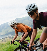 Women's Dusty Amber LunaLUXE Classic Cycling Jersey on road bike, breathable SPF50 moisture-wicking fabric, four-way stretch, extended sleeves, low-cut collar, silicone hem gripper, form-fitting performance