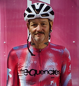 Frequencies Men's Classic Cycling Jersey (Fusca) in pink-red worn by rider in white helmet — LunaLUXE breathable SPF50, moisture-wicking, four-way stretch fabric, extended sleeves, low-cut collar and silicone gripper hem, Adelaide Frequencies 2026 logo; road cycling/training jersey.