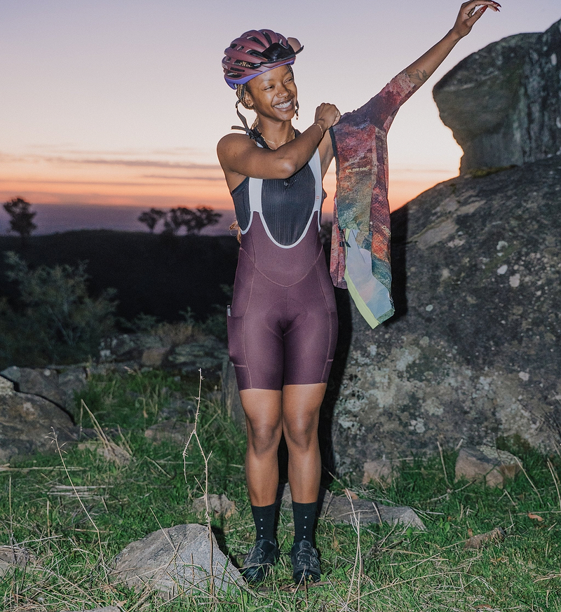 Pedla SuperSYSTEM women's fig cycling bib shorts close-up on rider at sunset, compressive Superfit fabric, high-density EIT chamois, silicone leg grippers, integrated hydration pocket and side stash pockets, for endurance gravel and road rides
