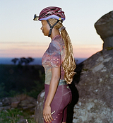 Side-profile of woman wearing ON_OFF GRID SuperSYSTEM women's ultralight short-sleeve cycling jersey and matching bib shorts with helmet, breathable moisture-wicking gravel and road kit with hydration tube channel and reflective accents