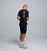 Side profile of the Men's Pro Pursuit Crit Suit – Black, showing sculpted sleeve panels with AeroPRISMA fabric, silicone leg grippers, and ergonomic design for high-speed movement.