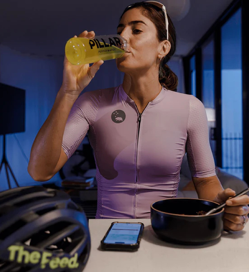 Cyclist in performance kit drinking Pillar Performance ULTRA IMMUNE C tropical powder from a yellow bottle — immune support performance nutrition with 1000mg Vitamin C, 15mg Zinc, 1000 IU Vitamin D3; sugar-free, vegan, Informed Sport certified, made in Australia.